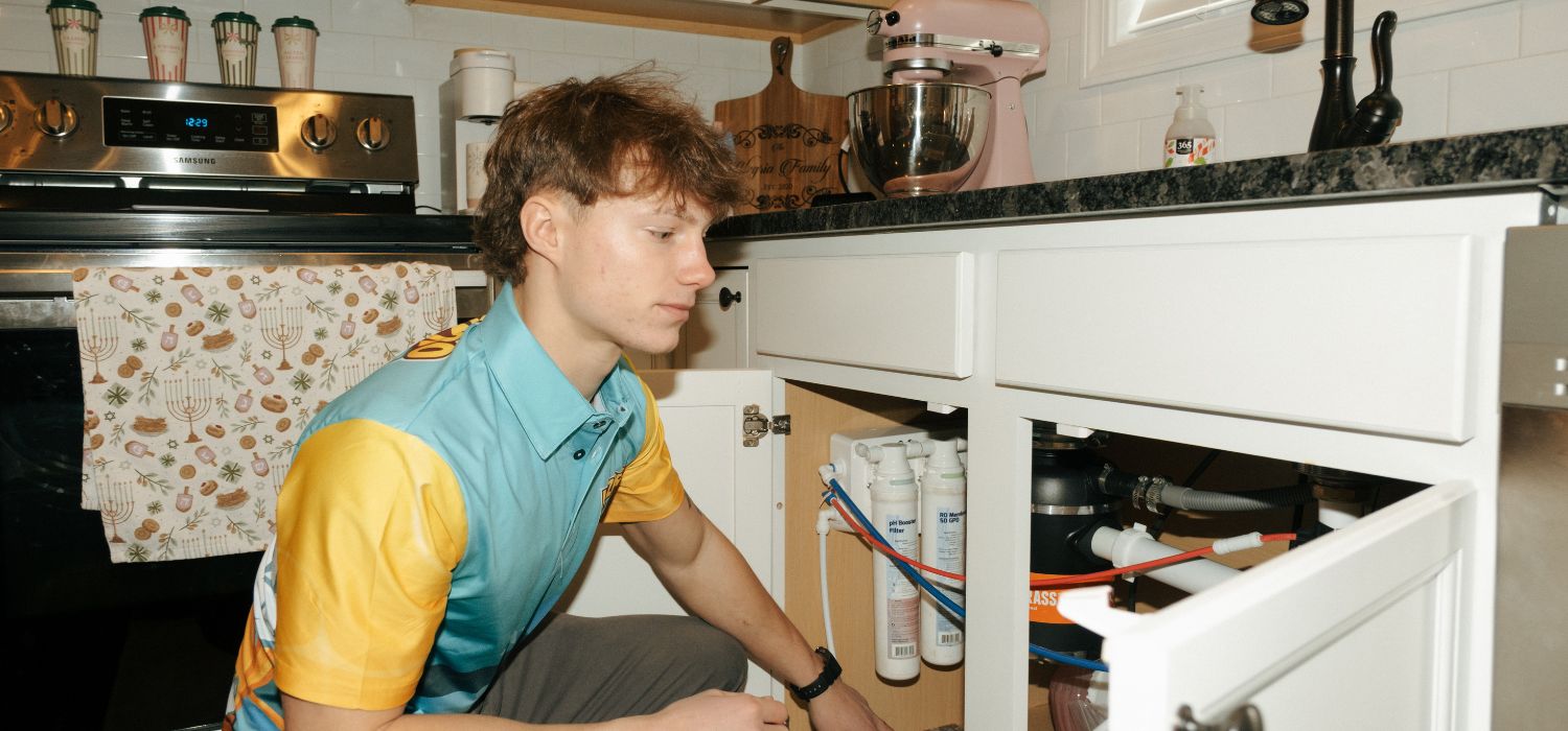 WHiZPRO PLUMBER technician installing or inspecting an under-sink water filtration system in a modern kitchen in Knoxville, TN.