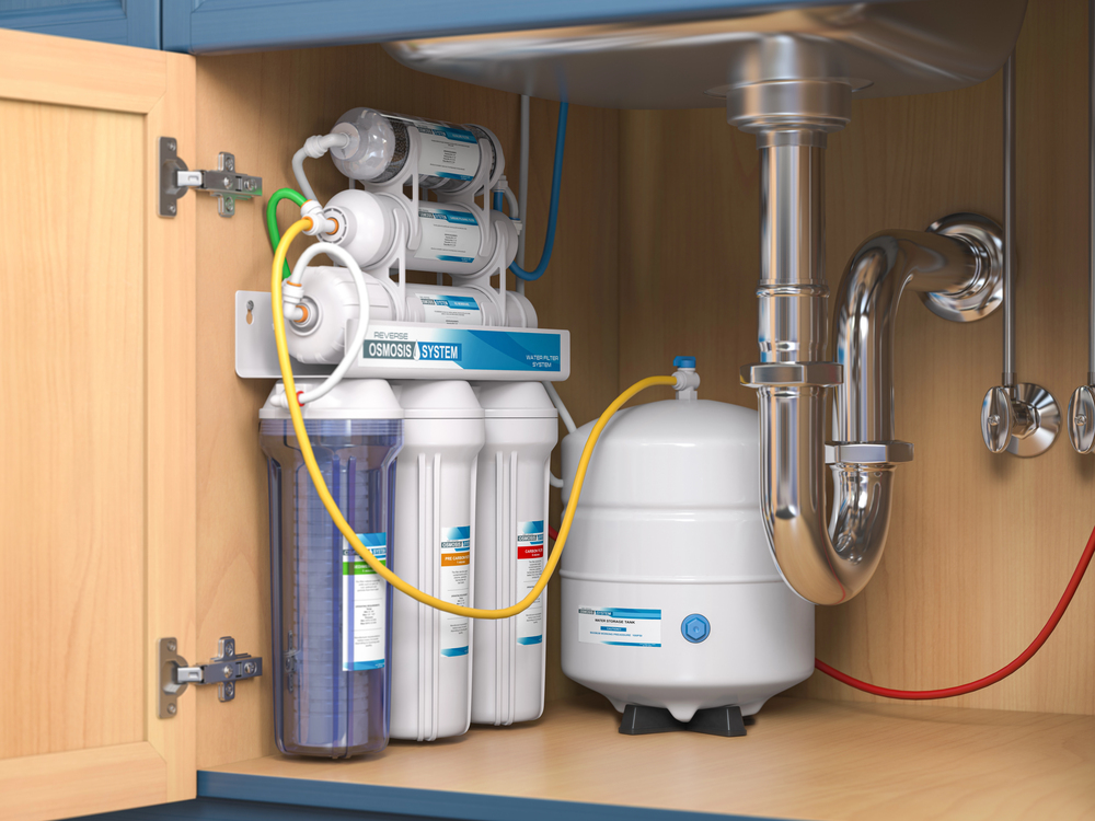 Reverse osmosis water filtration system installed under a kitchen sink, showing multiple filter cartridges, tubes, and a water storage tank.